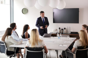 Mature Businessman Addressing Group Meeting Around Table At Graduate Recruitment Assessment Day #image_title